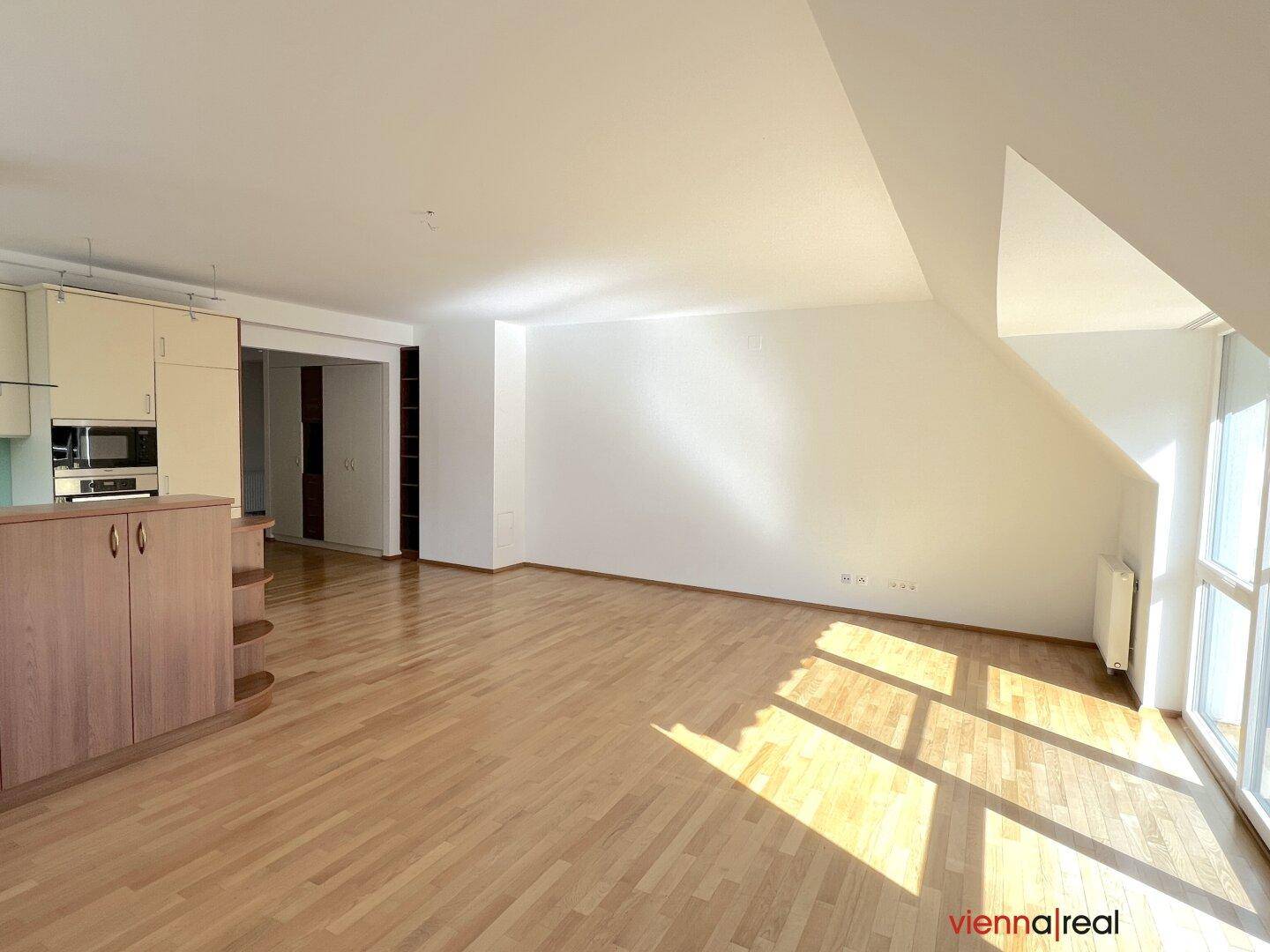 Geräumiger Wohnbereich mit Holzboden, Dachschrägen und integrierter Küchenzeile.