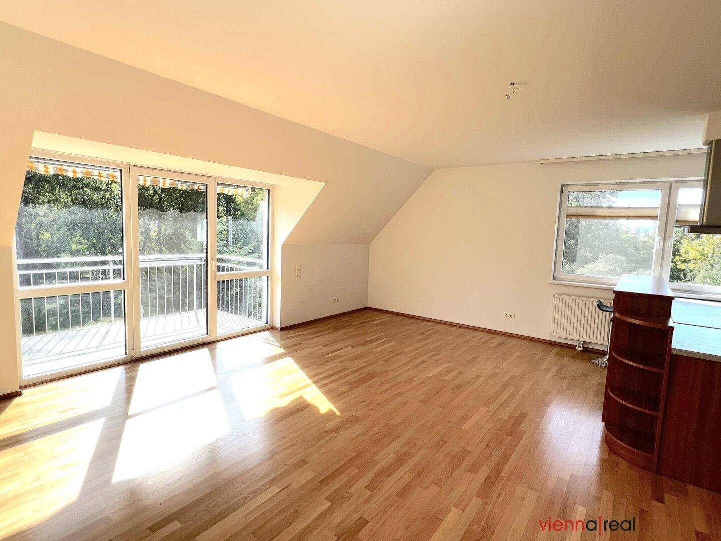 Sonniger Wohnbereich mit Holzboden, Dachschrägen und Blick ins Grüne vom Balkon.