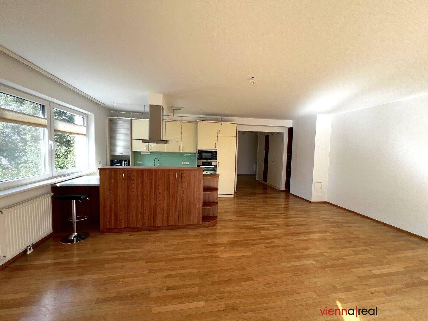 Offener Wohnbereich mit Küchenzeile, Holzboden und Fenstern mit Blick ins Grüne.