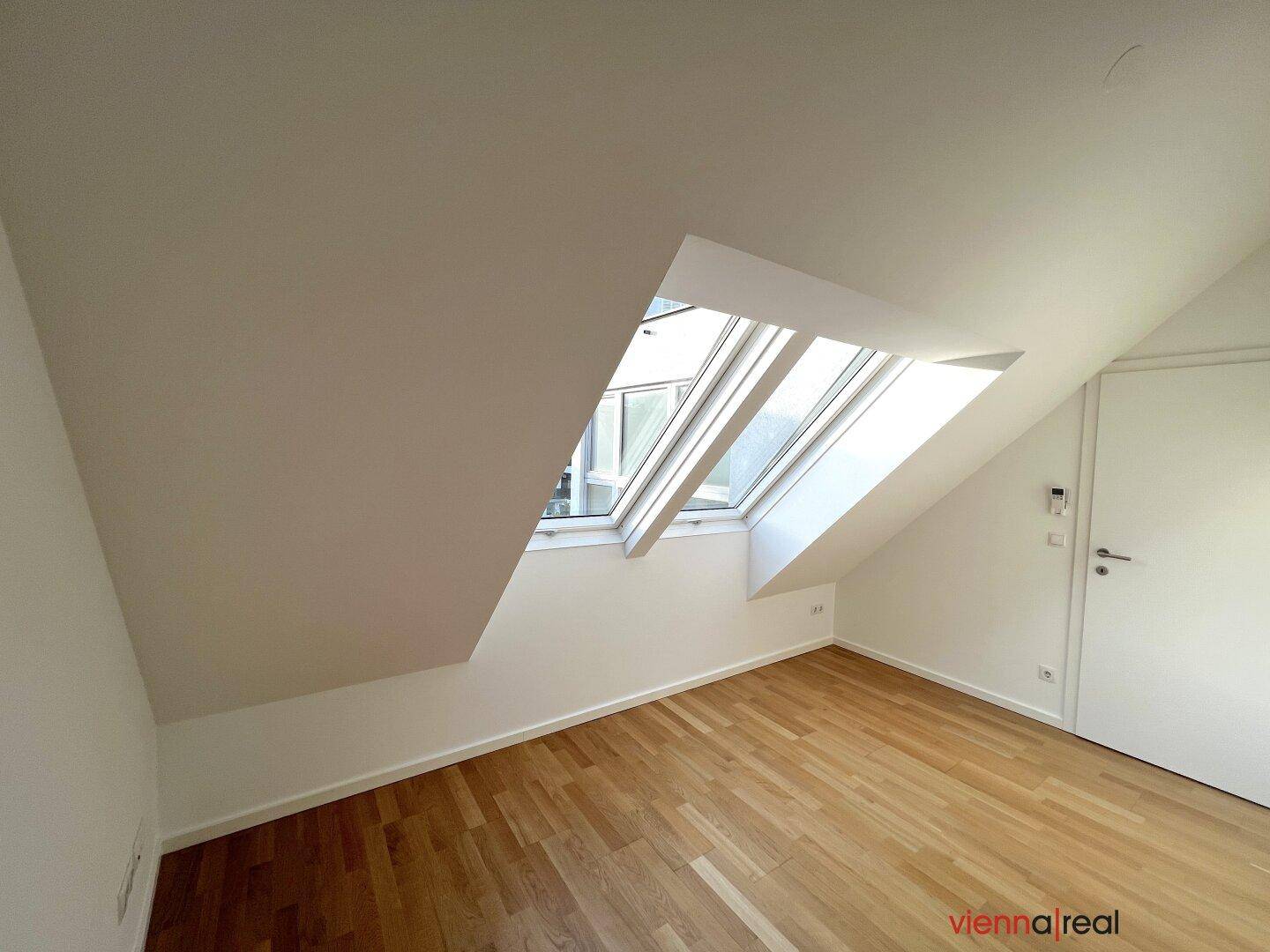 Heller Raum mit Holzboden, weißen Wänden und einem großen Dachfenster in der Schräge.