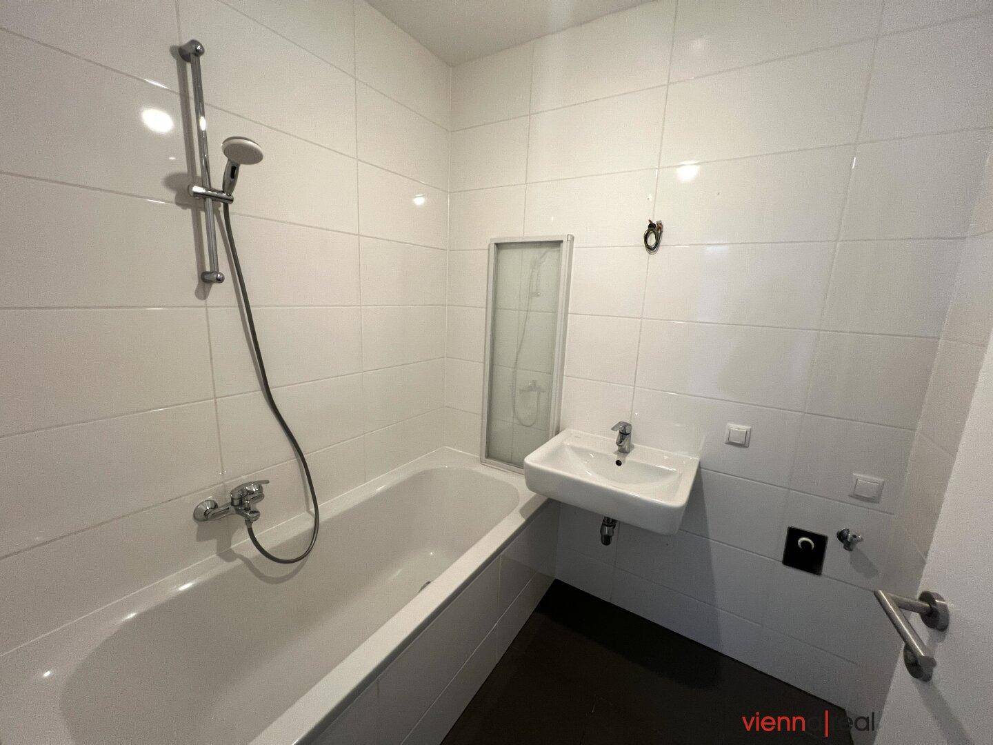 Modernes Badezimmer mit weißen Wandfliesen, Badewanne mit Duschfunktion und Einzelwaschbecken.