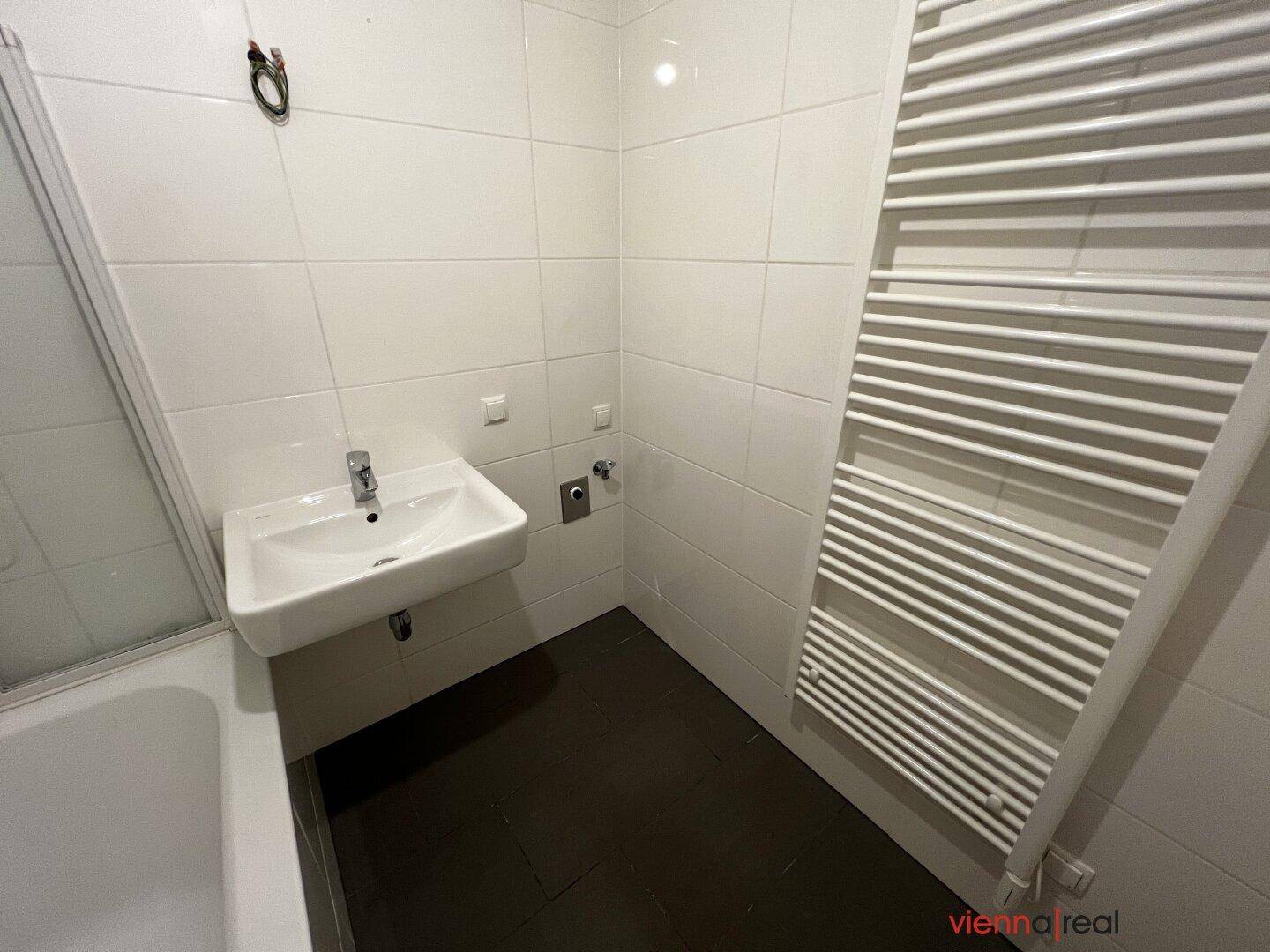 Modernes Badezimmer mit weißen Fliesen, Einzelwaschbecken und beheiztem Handtuchhalter.