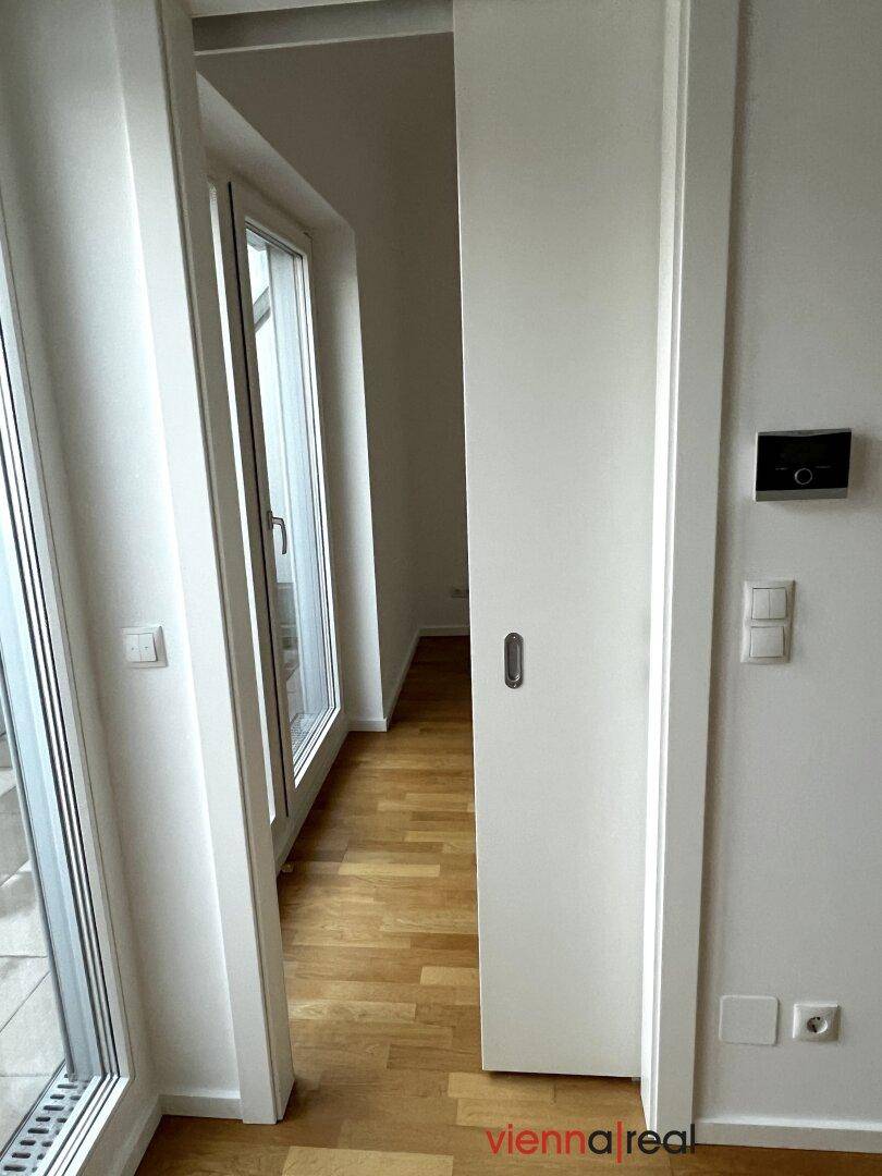 Heller Flur mit Holzboden und großen Glastüren, die zum Außenbereich führen.