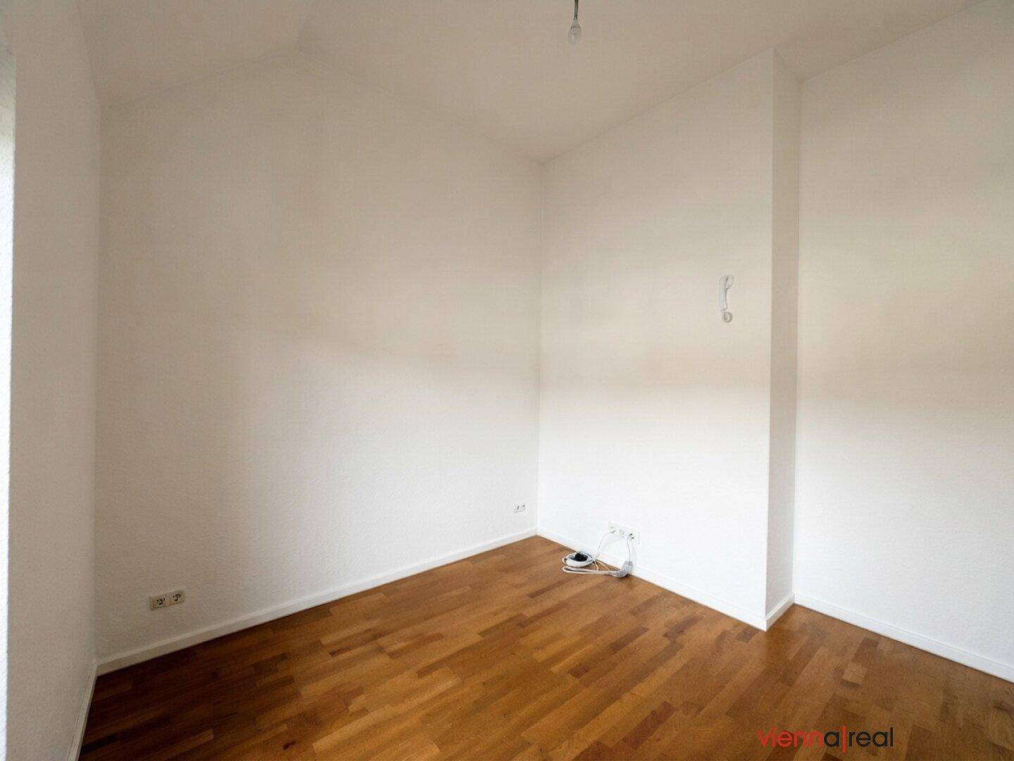 Weiterer Blick in den leeren Raum mit Holzboden und sauberen weißen Wänden.