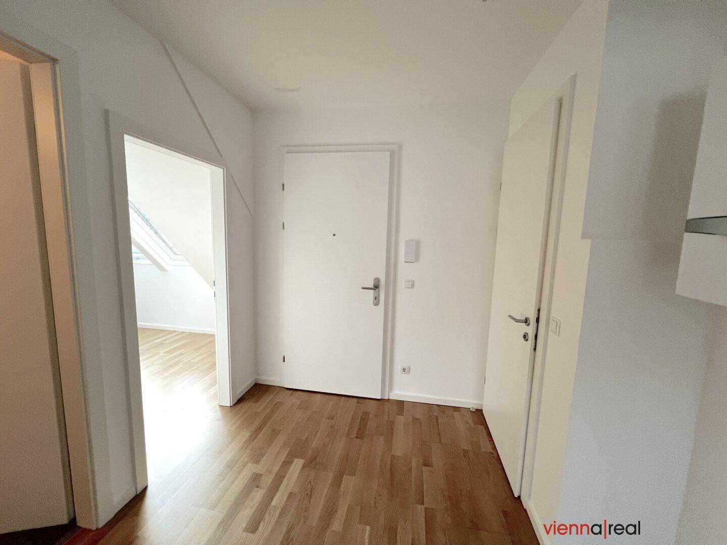 Heller Eingangsbereich mit Holzboden und weißen Türen, führt zu den angrenzenden Räumen.