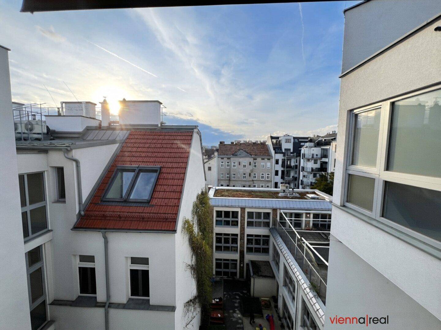 Sonniger Ausblick auf Dächer, umliegende Gebäude und einen begrünten Innenhof.