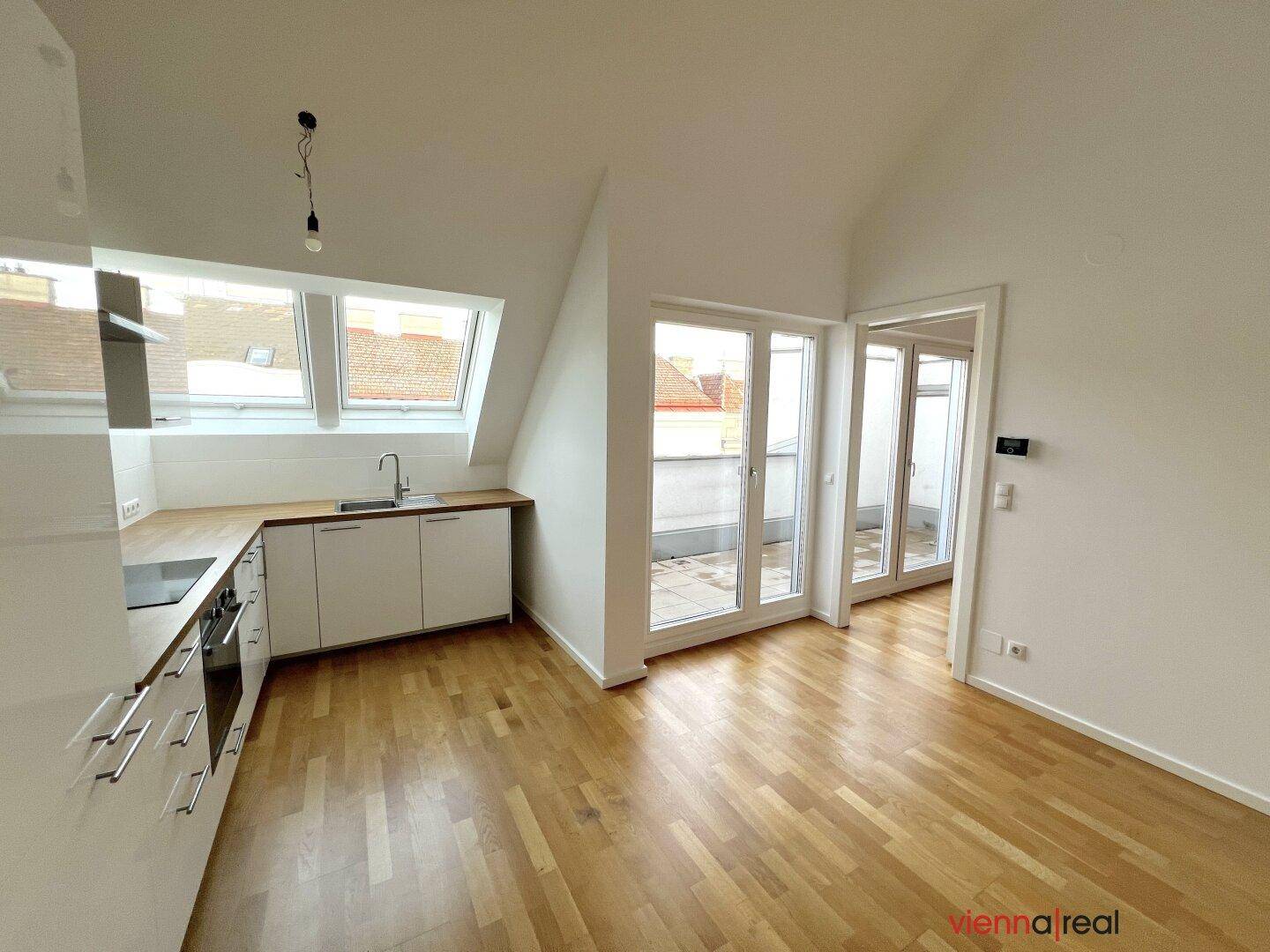 Heller Küchenbereich mit Holzboden, weißen Wänden und großen Fenstern mit Zugang zu einem Außenbereich.