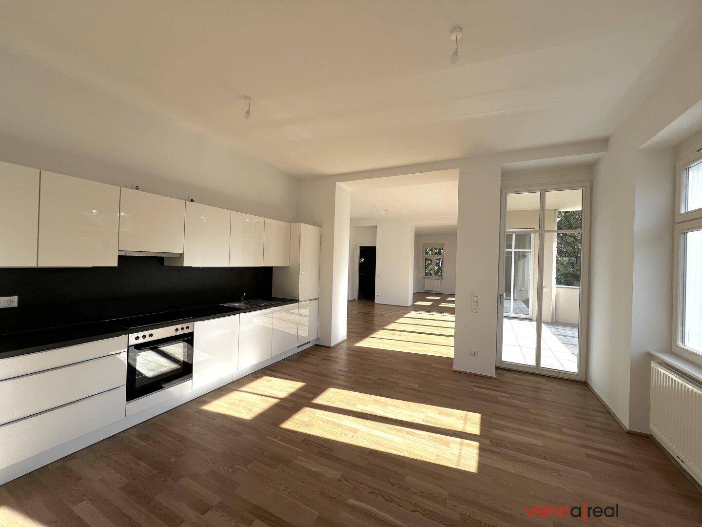 Offener Wohnbereich mit integrierter Küche, Parkettboden und Zugang zum sonnigen Balkon.