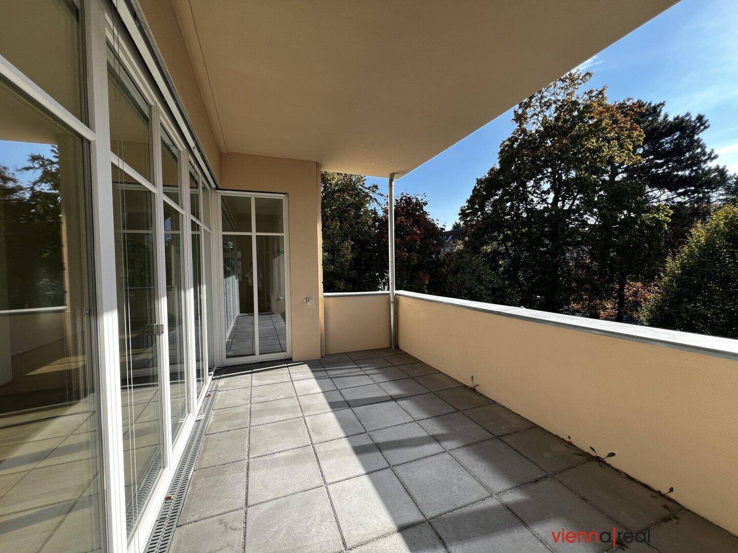 Langer Balkon mit Fliesenboden und großen Fenstern, die viel Licht in den Innenraum lassen.