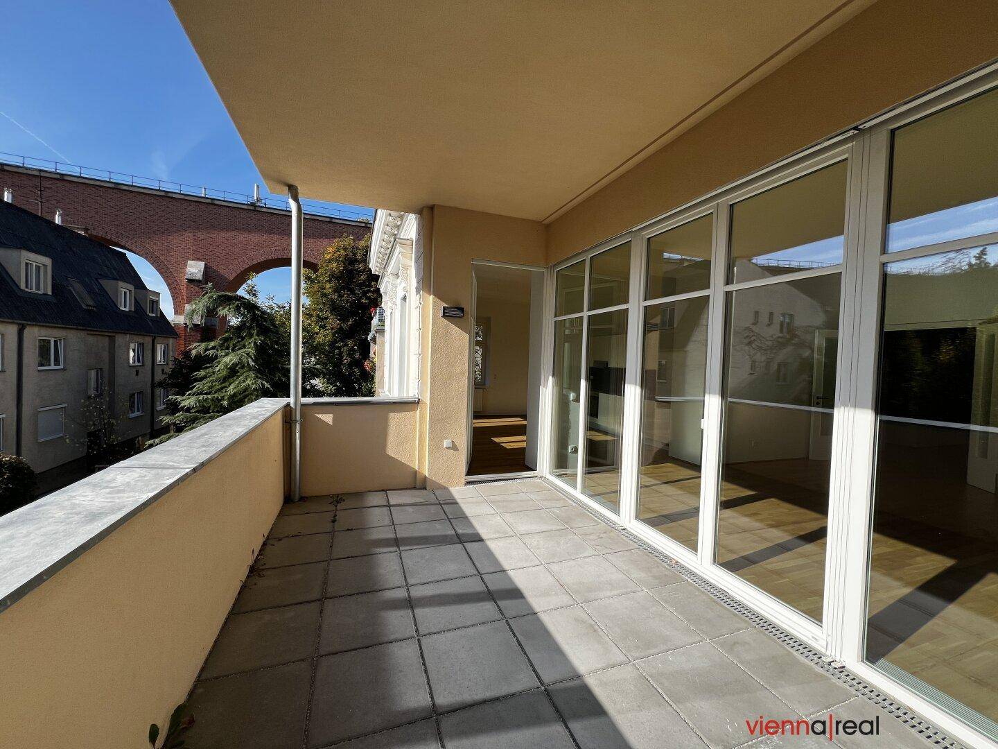 Sonniger Balkon mit Fliesenboden und Blick auf eine historische Brücke in der Ferne.