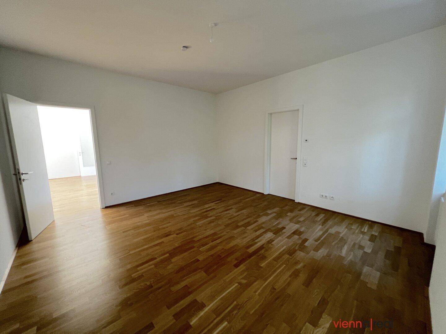 Geräumiges Zimmer mit hellem Parkettboden und Zugang zu weiteren Räumen.