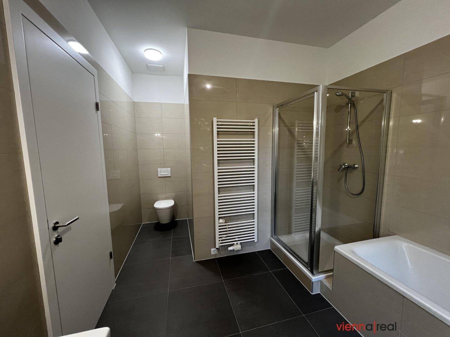 Funktionales Badezimmer mit Duschkabine, WC, beheiztem Handtuchhalter und modernen Fliesen.