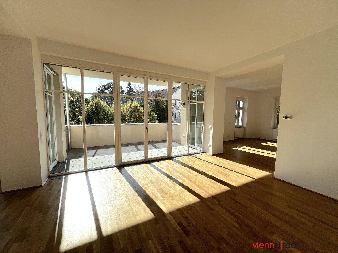 Helles Wohnzimmer mit Parkettboden und großen Glasfronten, die zum sonnigen Balkon führen.