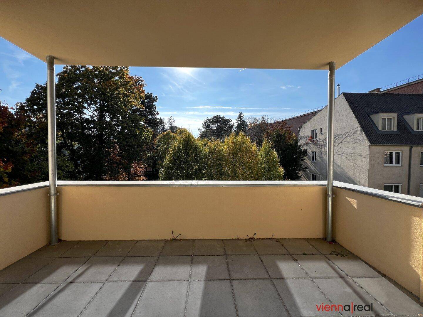 Geräumiger Balkon mit Fliesenboden und weitem Blick ins Grüne unter blauem Himmel.