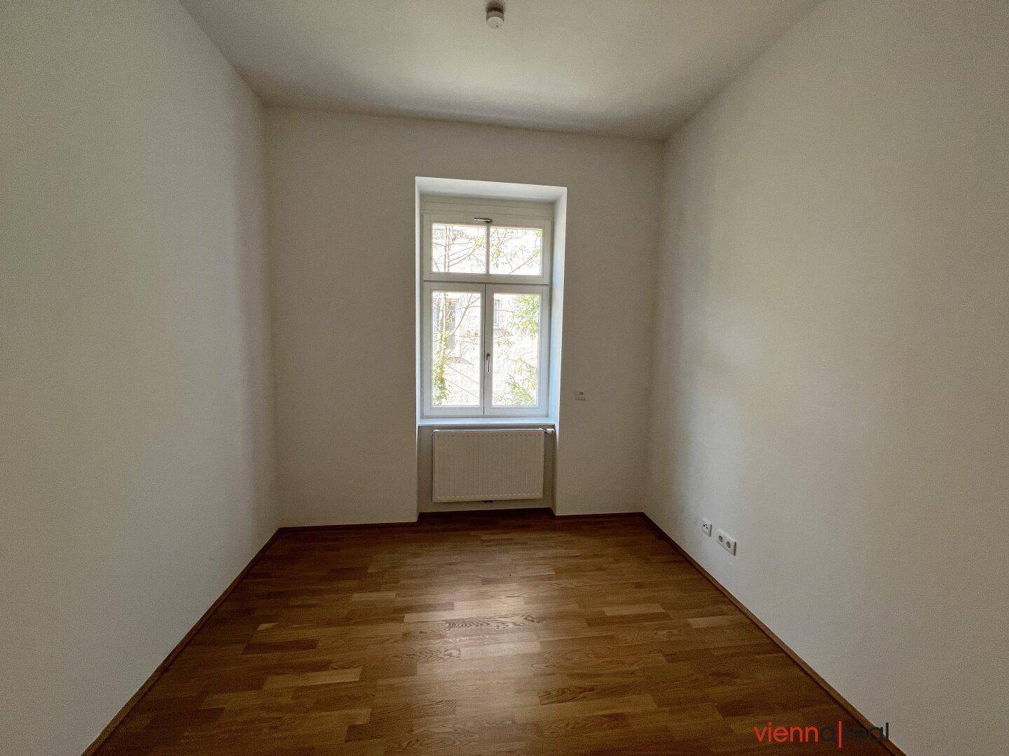 Helles Zimmer mit Parkettboden und einem Fenster, bietet eine ruhige Atmosphäre.