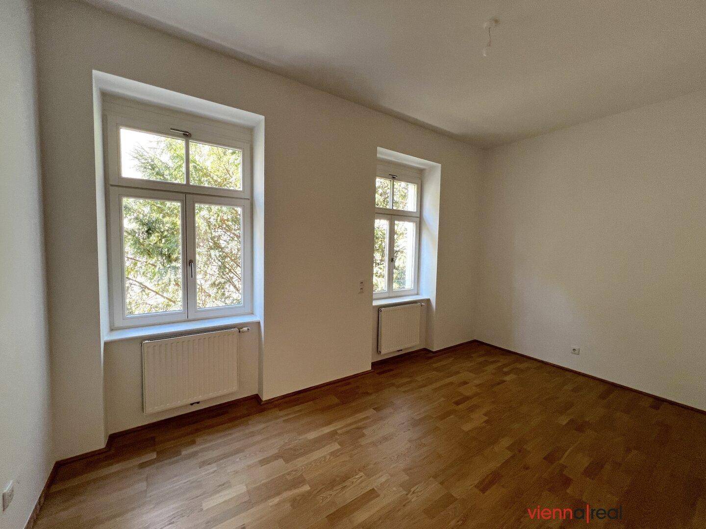 Heller Raum mit zwei Fenstern und Parkettboden, bietet viel Tageslicht.