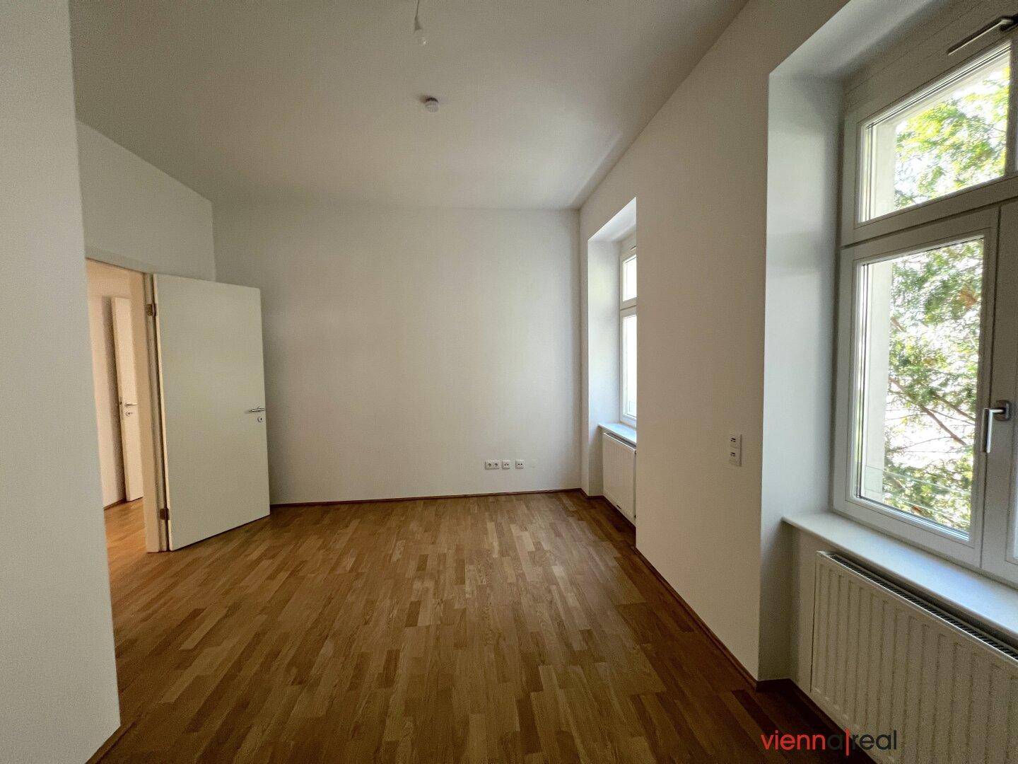 Lichtdurchflutetes Zimmer mit Parkettboden und mehreren Fenstern, bietet eine angenehme Atmosphäre.