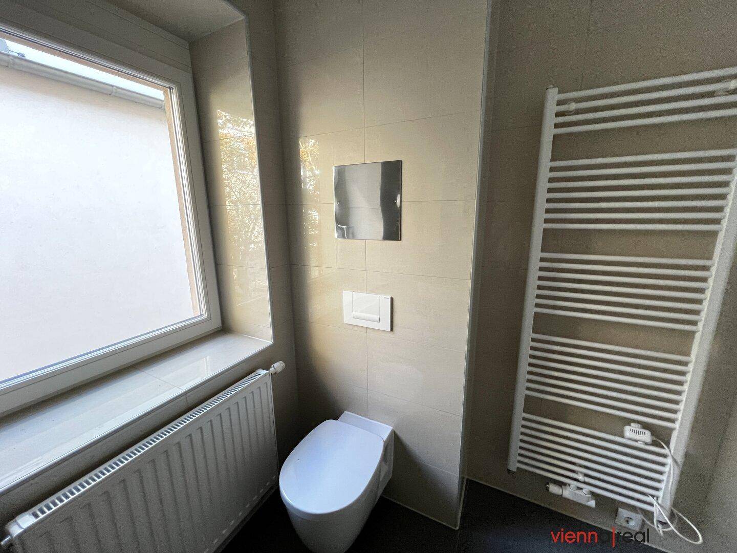 Separates WC mit wandhängender Toilette, beheiztem Handtuchhalter und Fenster.