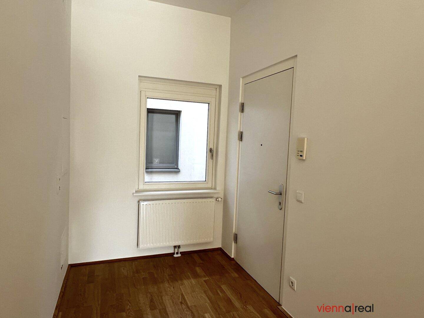 Eingangsbereich mit Parkettboden, Fenster und weißer Eingangstür, hell und einladend.