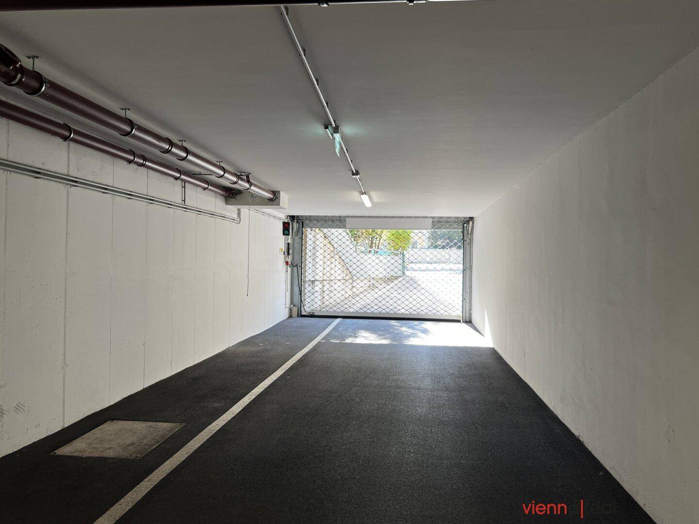 Tiefgaragenzufahrt mit Rolltor und heller Beleuchtung, die ins Freie führt.