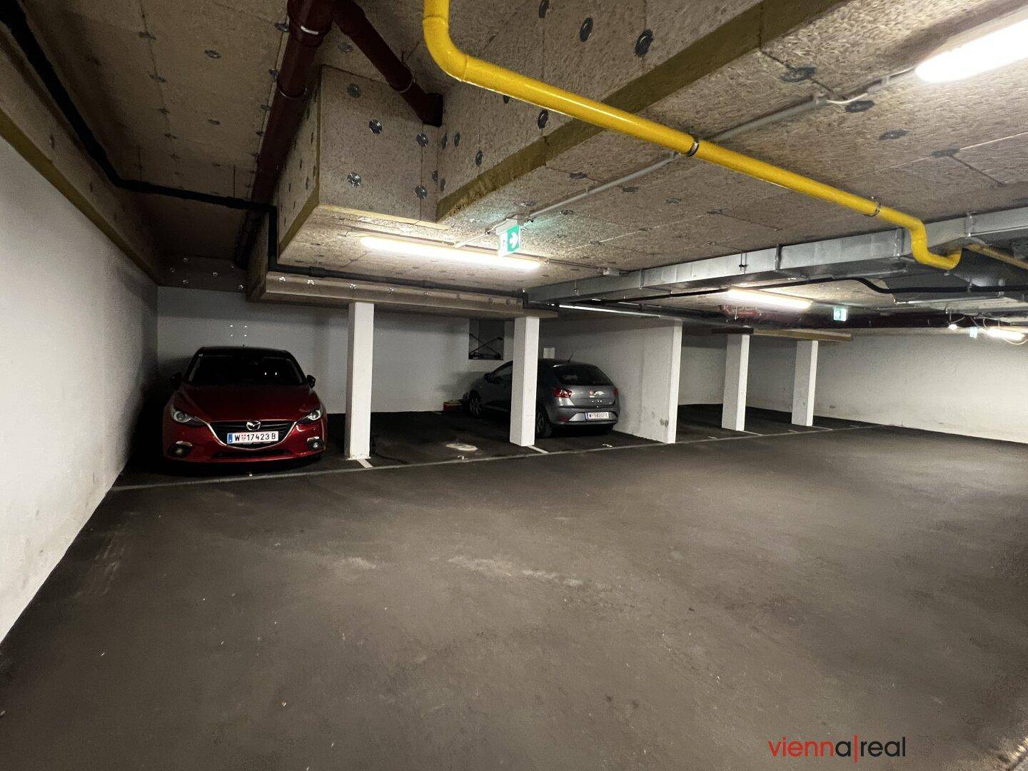 Tiefgarage mit mehreren Stellplätzen und sichtbaren Versorgungsleitungen an der Decke.