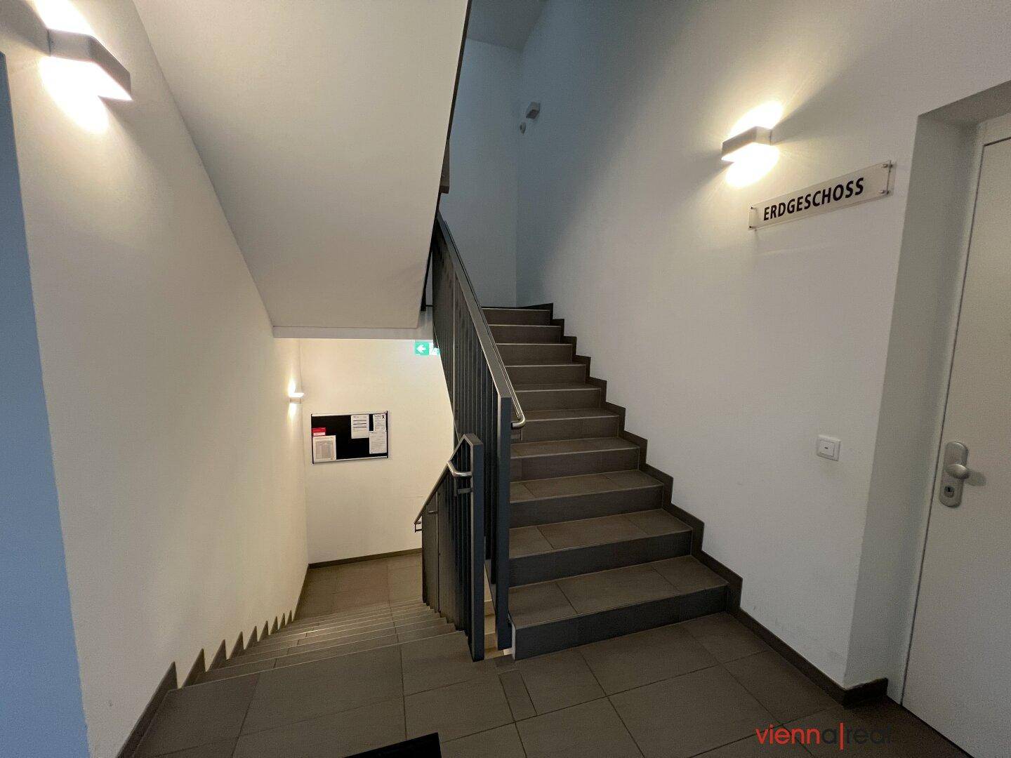 Modernes Treppenhaus mit Fliesenstufen, Metallgeländer und heller Wandgestaltung.
