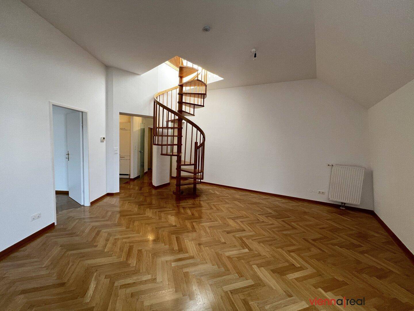 Heller Wohnbereich mit elegantem Fischgrätparkett und einer markanten Holzwendeltreppe unter einem Oberlicht.