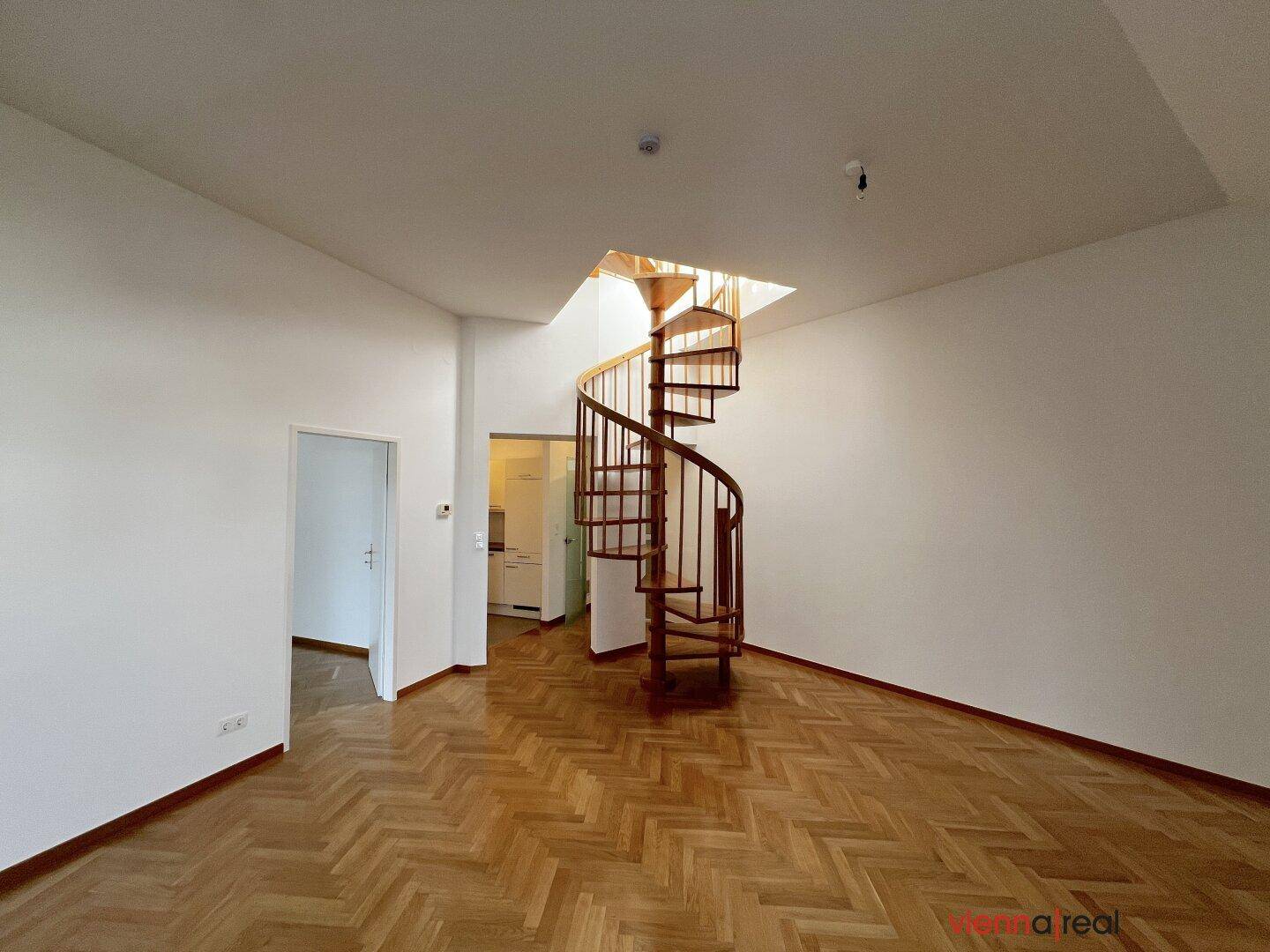 Heller Wohnbereich mit Fischgrätparkett, weiß gestrichenen Wänden und einer Holzwendeltreppe mit Oberlicht.