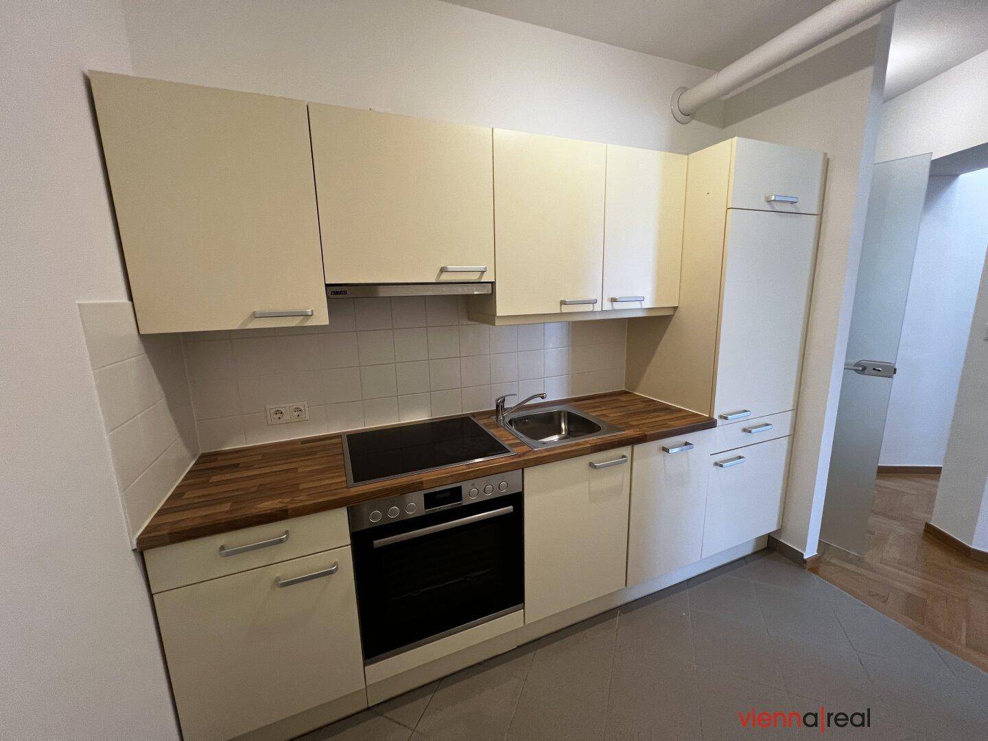 Detailansicht der Küche mit Kochfeld, Spüle, hellen Schränken und Holz-Arbeitsplatte.