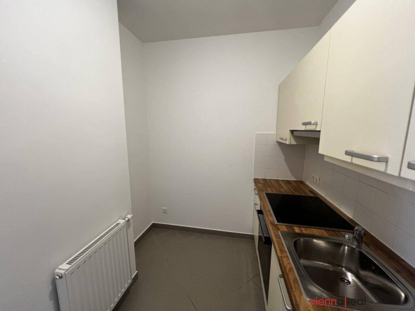 Blick in die kompakte Küche mit Heizkörper, hellen Schränken und Holzarbeitsplatte.