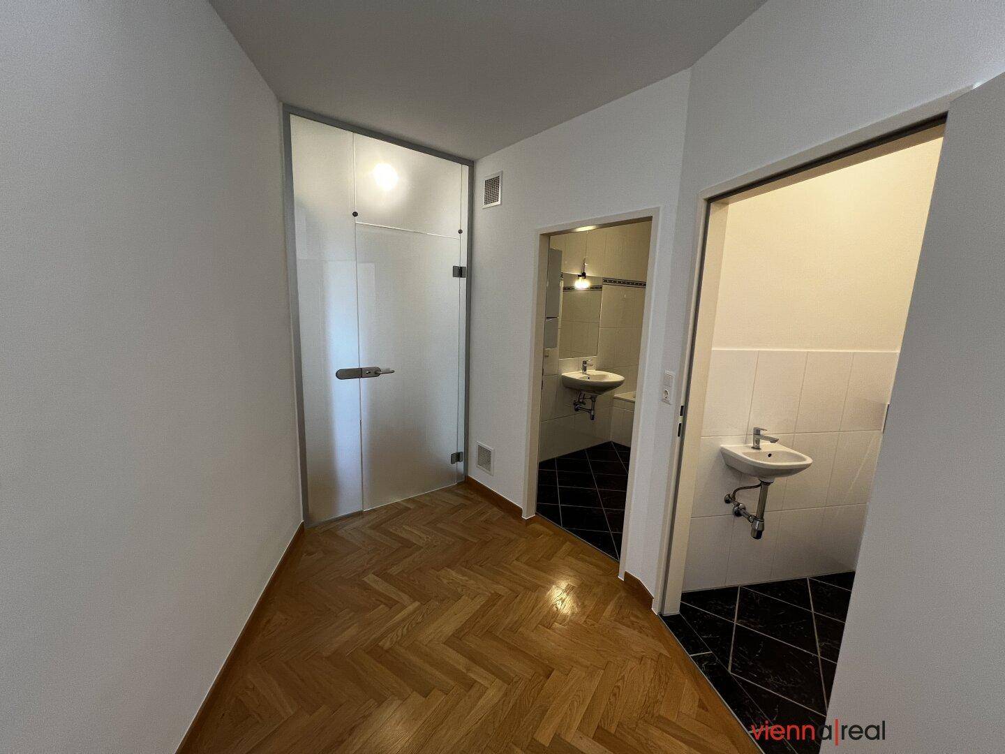 Flur mit Fischgrätparkett, einer Milchglastür und Zugang zu einem gefliesten Gästebereich.