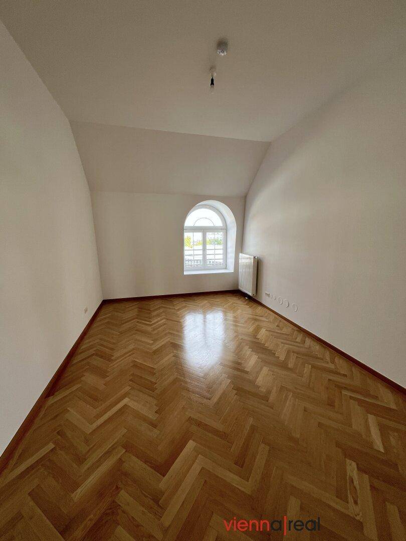 Helles Schlafzimmer mit Fischgrätparkett, weißen Wänden und einem charmanten Rundbogenfenster.