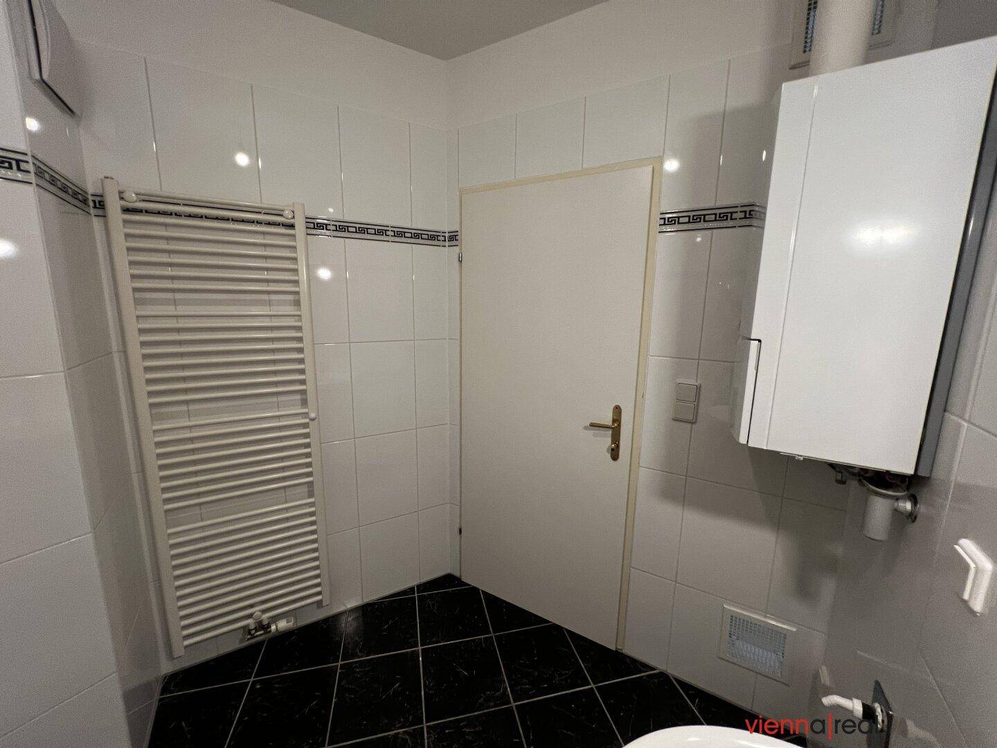 Badezimmer mit weißen Wandfliesen, schwarzen Bodenfliesen und einem praktischen Handtuchheizkörper.