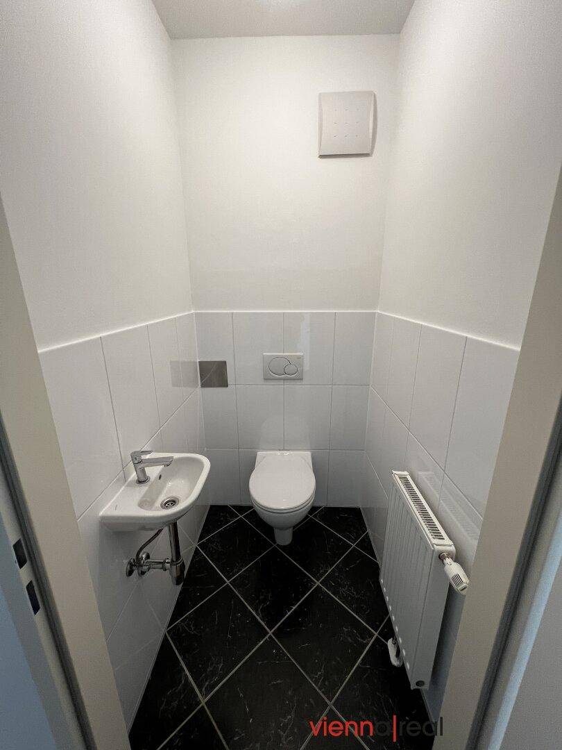 Kleines WC mit weißen Wandfliesen, schwarzen Bodenfliesen, wandhängendem WC und Handwaschbecken.