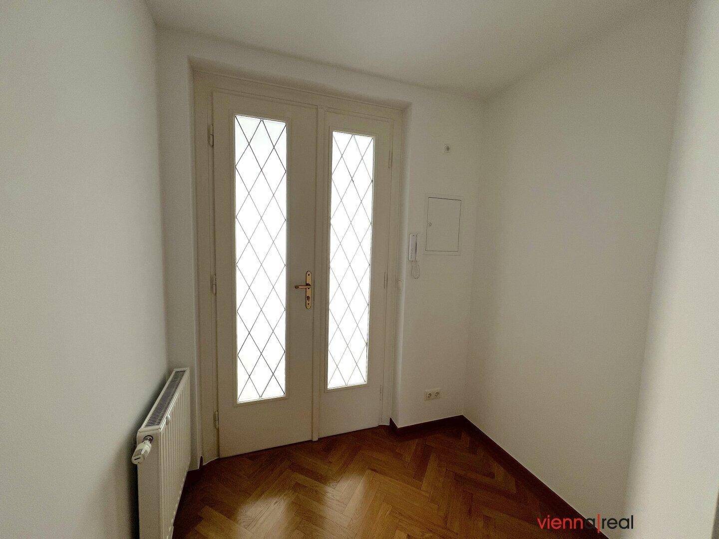 Eingangsbereich mit Fischgrätparkett und einer eleganten Doppeltür mit Rautenmuster.