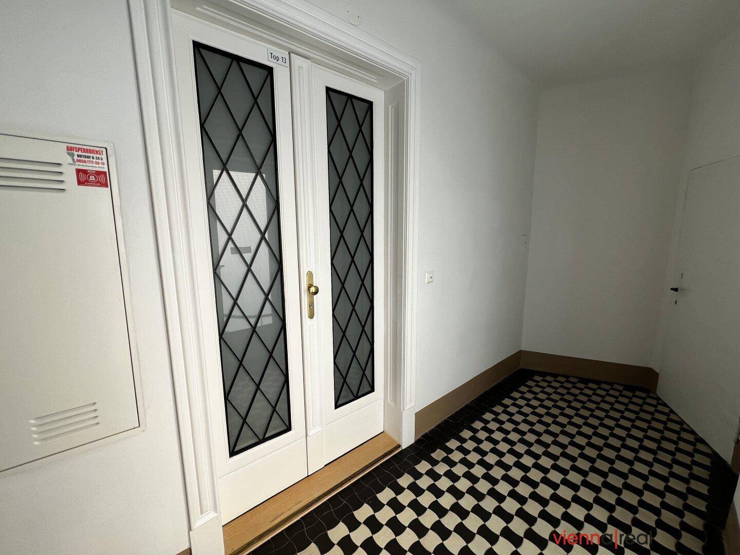 Eingangsbereich mit schwarz-weißem Schachbrettmuster-Fliesenboden und Doppeltür.