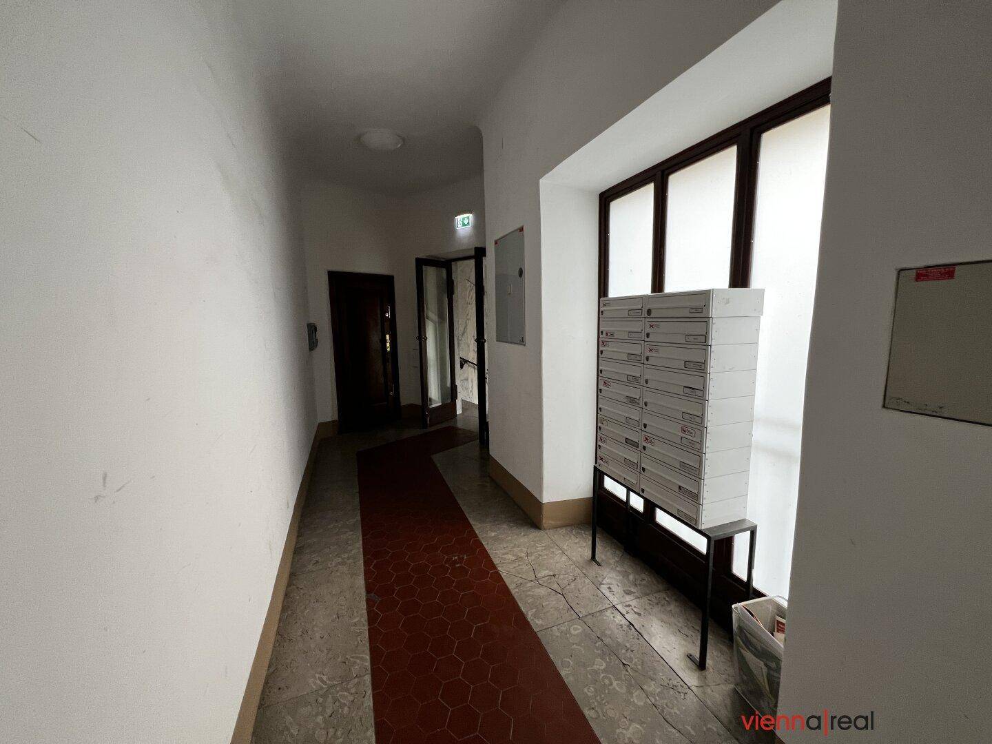 Langer Flur im Eingangsbereich eines Gebäudes mit Briefkästen und Fenster.