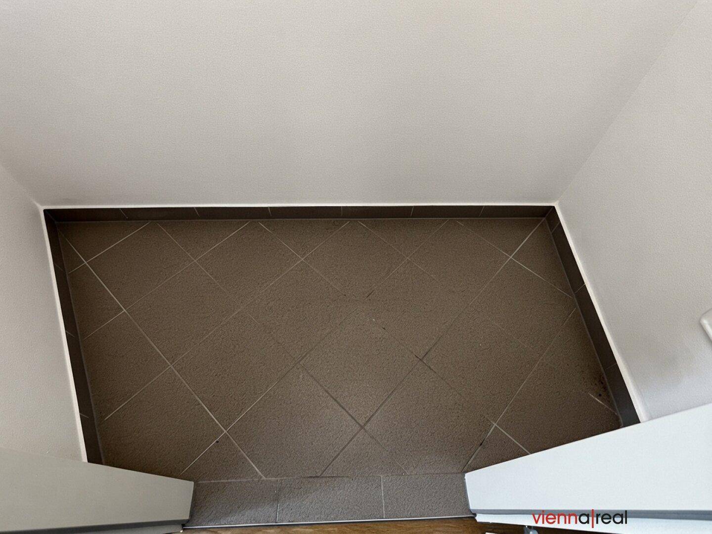 Nahaufnahme eines kleinen, leeren Raumes mit diagonal verlegten Fliesen.