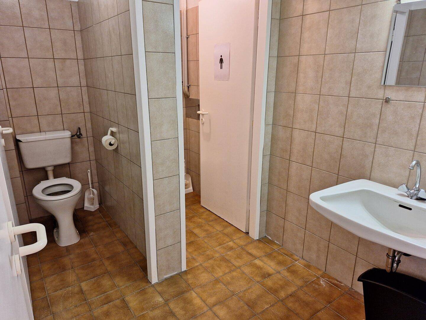 Einfache Toilettenanlage mit Fliesenboden und -wänden, ausgestattet mit WC und Waschbecken.
