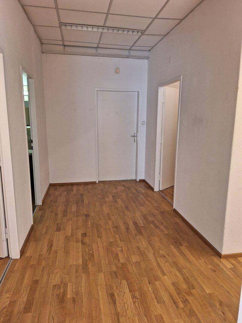 Langer Flur mit Holzparkettboden und mehreren Türen, der zu verschiedenen Räumen innerhalb des Gebäudes führt.