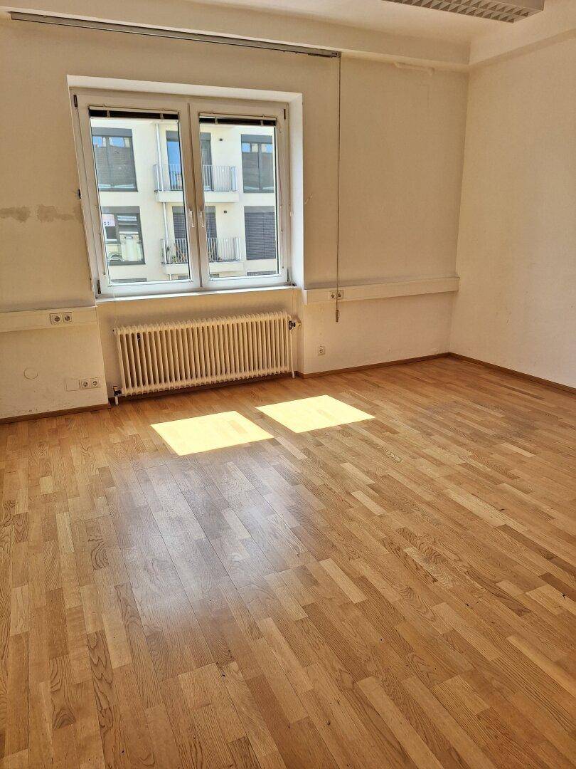 Büroraum mit hellem Parkettboden und einem großen Fenster, das einen Blick auf die umliegenden Gebäude bietet.