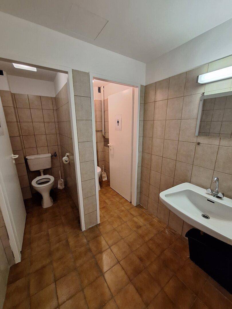 Mehrere Toilettenkabinen in einem gefliesten Raum mit Waschbecken und Spiegel, ideal für Büronutzung.