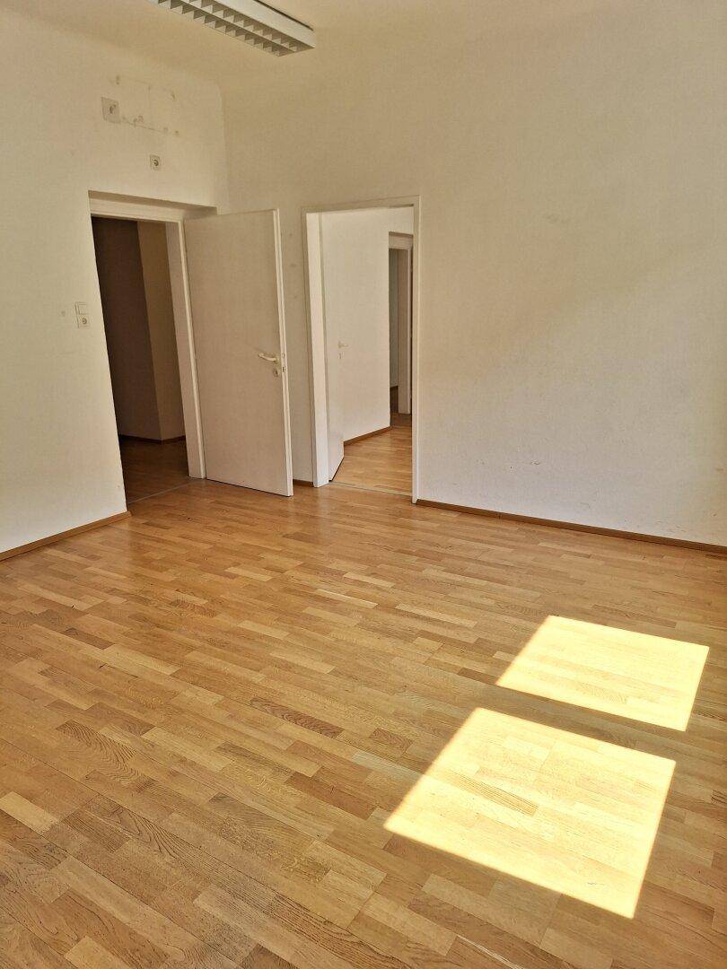 Geräumiger Büroraum mit hellem Parkettboden und mehreren Türen, die zu angrenzenden Bereichen führen.