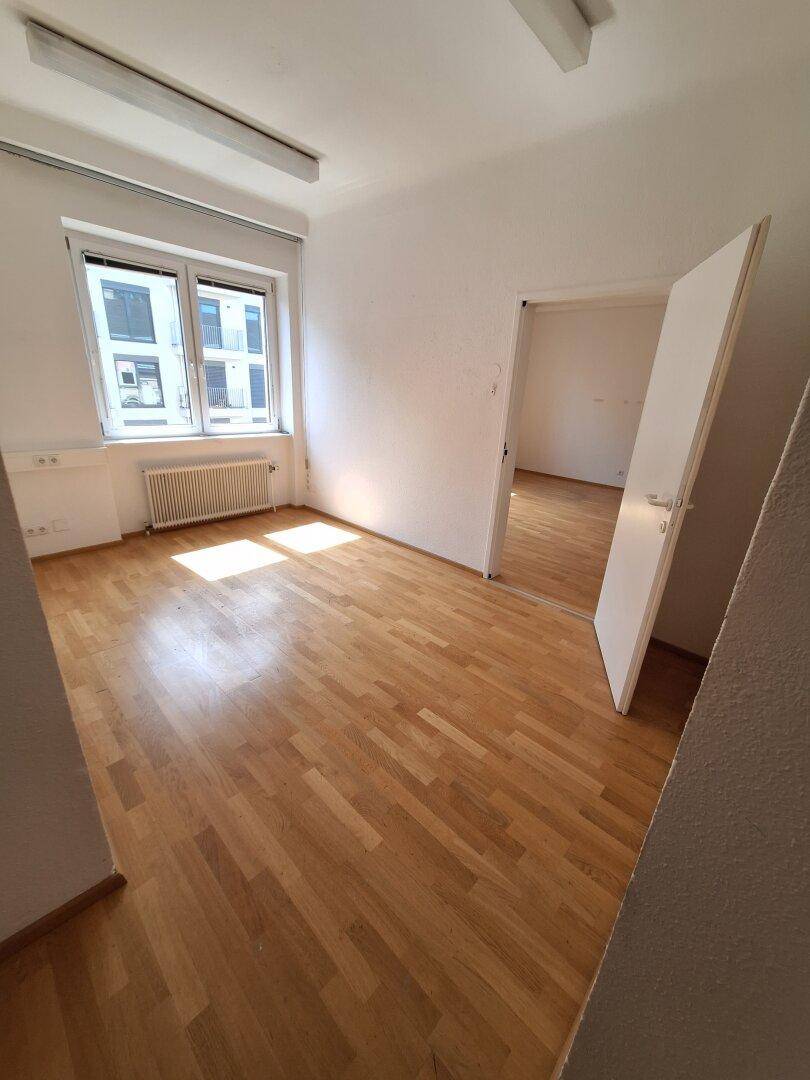 Heller Büroraum mit Parkettboden und einem Fenster, das den Raum mit Sonnenlicht durchflutet.