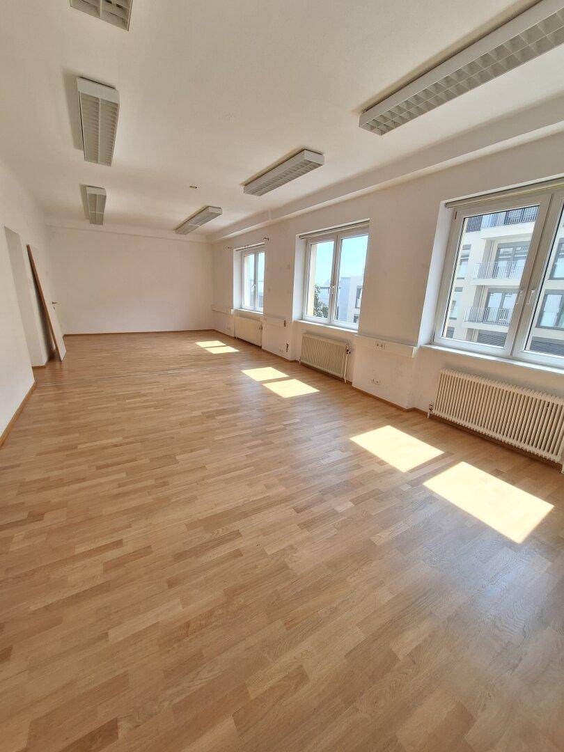 Langer Büroraum mit mehreren Fenstern, die den Raum mit natürlichem Licht durchfluten und eine helle Arbeitsumgebung schaffen.