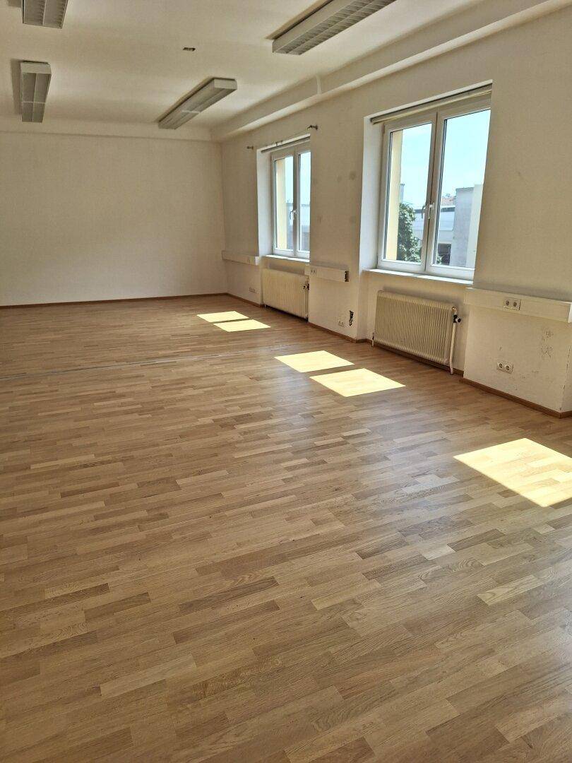 Langer Büroraum mit mehreren Fenstern, die den Raum mit natürlichem Licht durchfluten und eine helle Arbeitsumgebung schaffen.