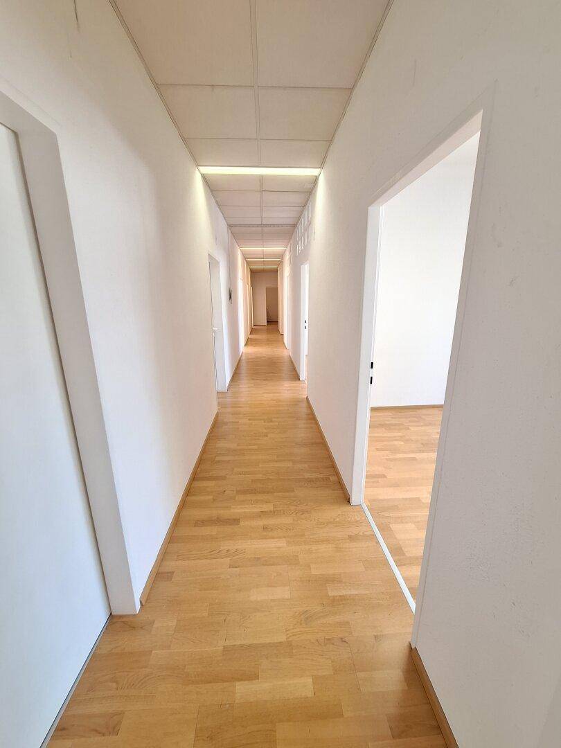 Langer Flur mit hellem Parkettboden und mehreren Türen, die zu den einzelnen Büroräumen führen.
