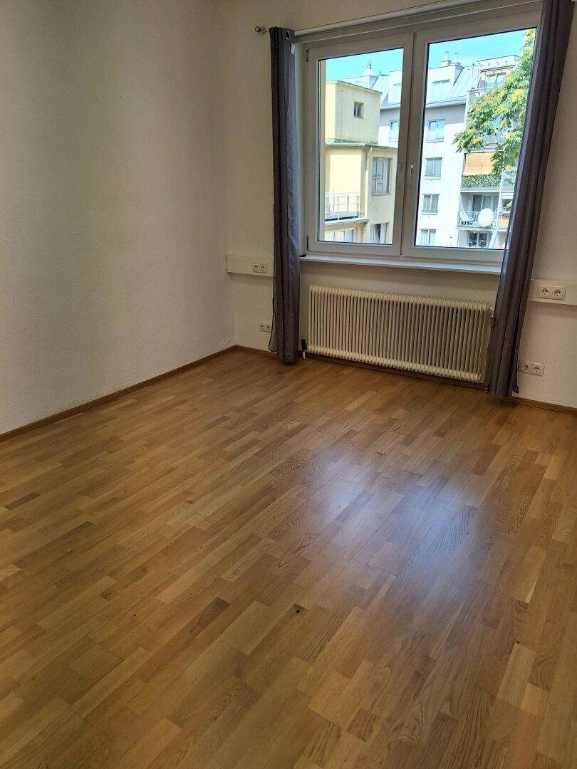 Büroraum mit hellem Parkettboden und einem großen Fenster, das den Raum mit natürlichem Licht erfüllt.