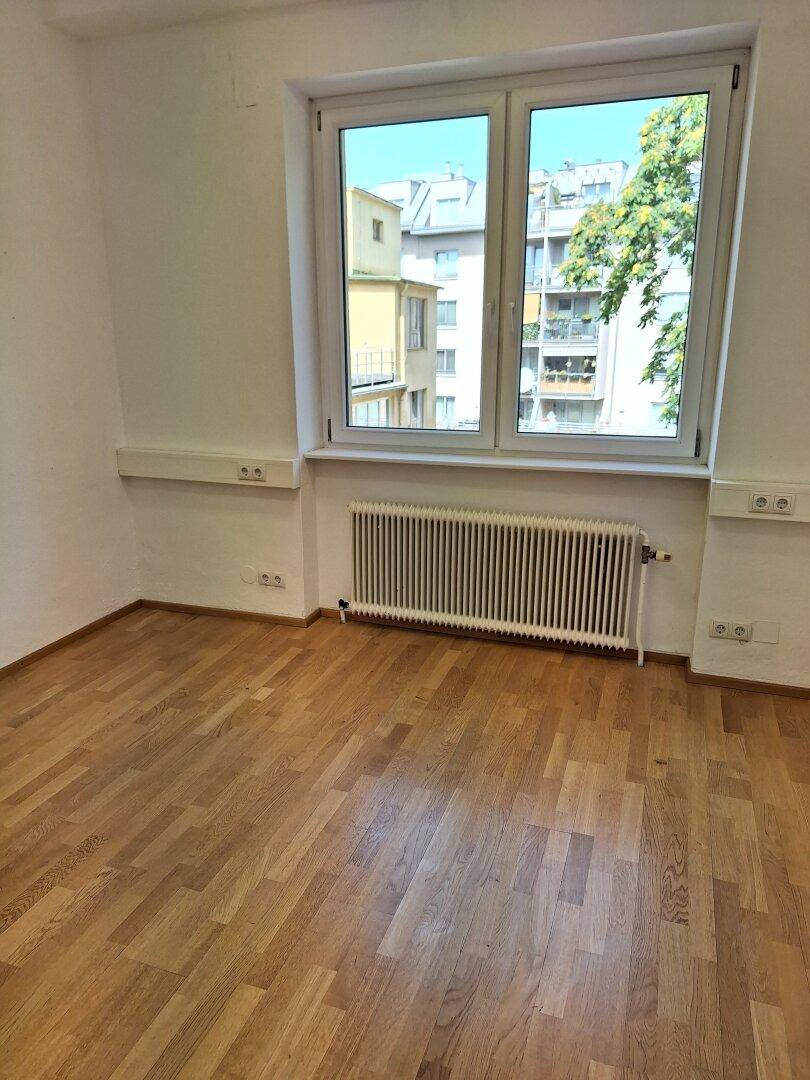Helles Büro mit Holzparkettboden und großem Fenster, das viel Tageslicht hereinlässt und einen Stadtblick bietet.
