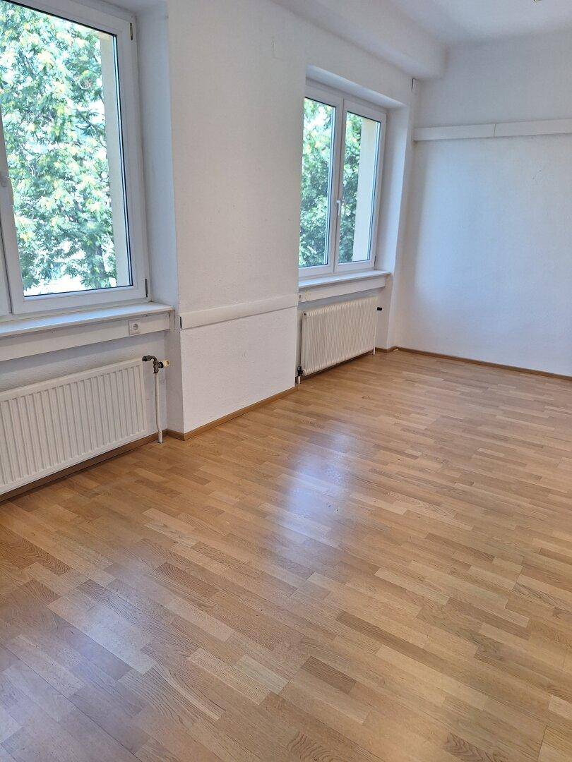 Heller Büroraum mit zwei Fenstern, die viel natürliches Licht spenden und einen angenehmen Blick ins Grüne bieten.